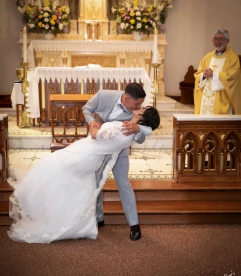 Wedding ceremony kiss at the altar — groom dipping bride for a kiss, officiant smiling in the background