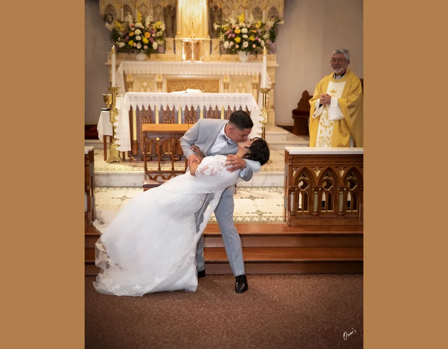 Wedding ceremony kiss at the altar — groom dipping bride for a kiss, officiant smiling in the background