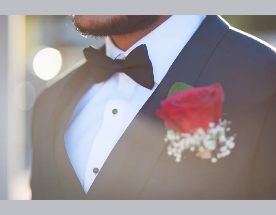 Groom's boutonniere detail shot — close-up of black bow tie and red rose boutonniere
