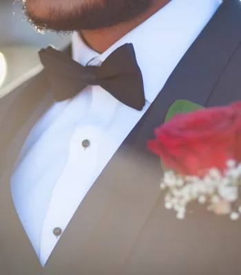 Groom's boutonniere detail shot — close-up of black bow tie and red rose boutonniere