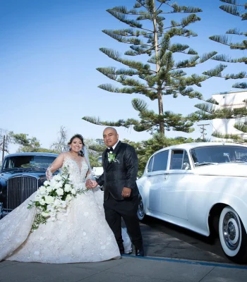 Wedding couple arriving in vintage cars — bride and groom walking past a classic vintage car outside the venue