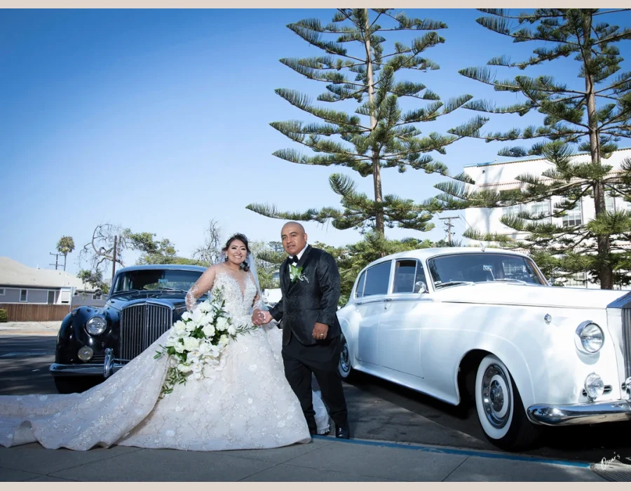 Wedding couple arriving in vintage cars — bride and groom walking past a classic vintage car outside the venue