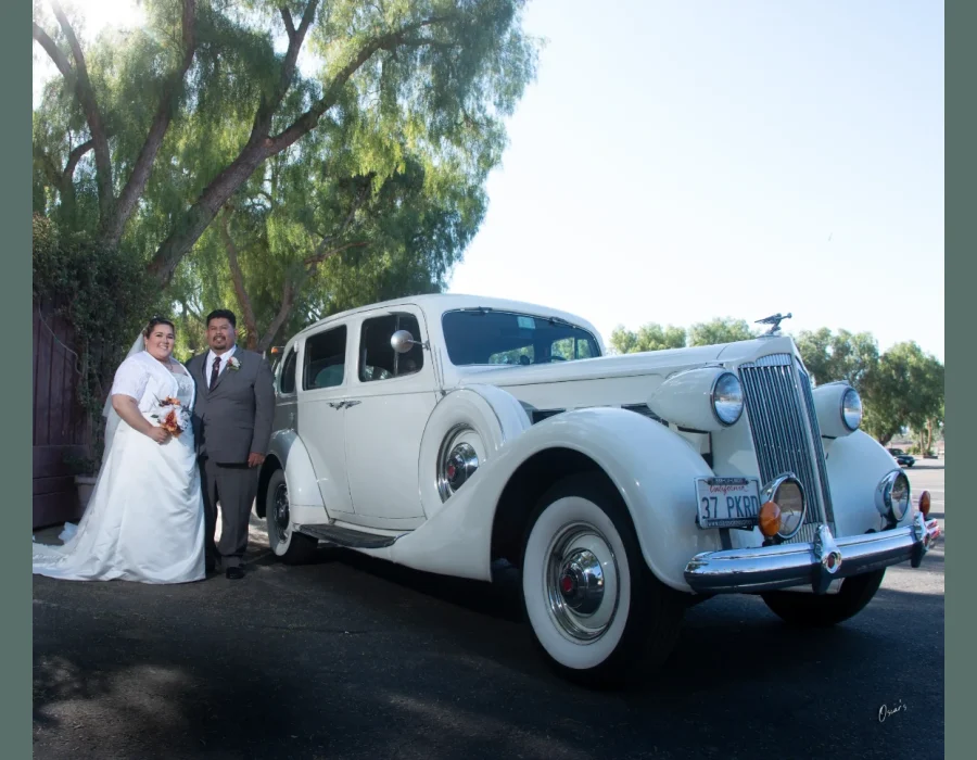 Wedding couple with vintage car — bride and groom posing beside a classic cream-colored vintage car