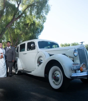 Wedding couple with vintage car — bride and groom posing beside a classic cream-colored vintage car