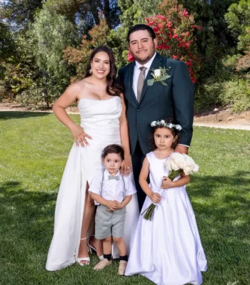 Wedding family portrait with children — bride and groom with a young boy and girl dressed in white, garden setting