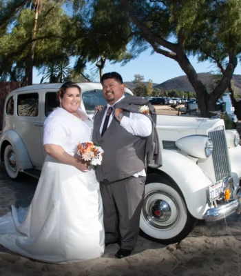 Wedding couple with vintage car (mountain backdrop) — bride and groom posing beside a vintage car with hills in the background