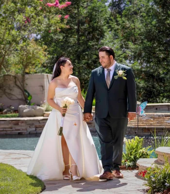Wedding couple walking by the pool — bride and groom holding hands, walking along a garden pool pathway