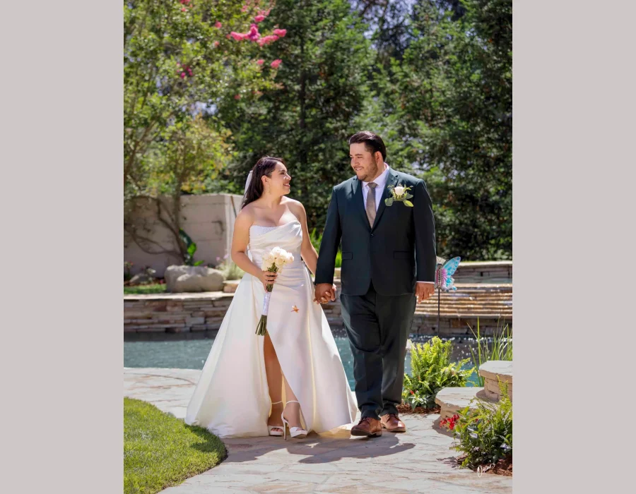 Wedding couple walking by the pool — bride and groom holding hands, walking along a garden pool pathway