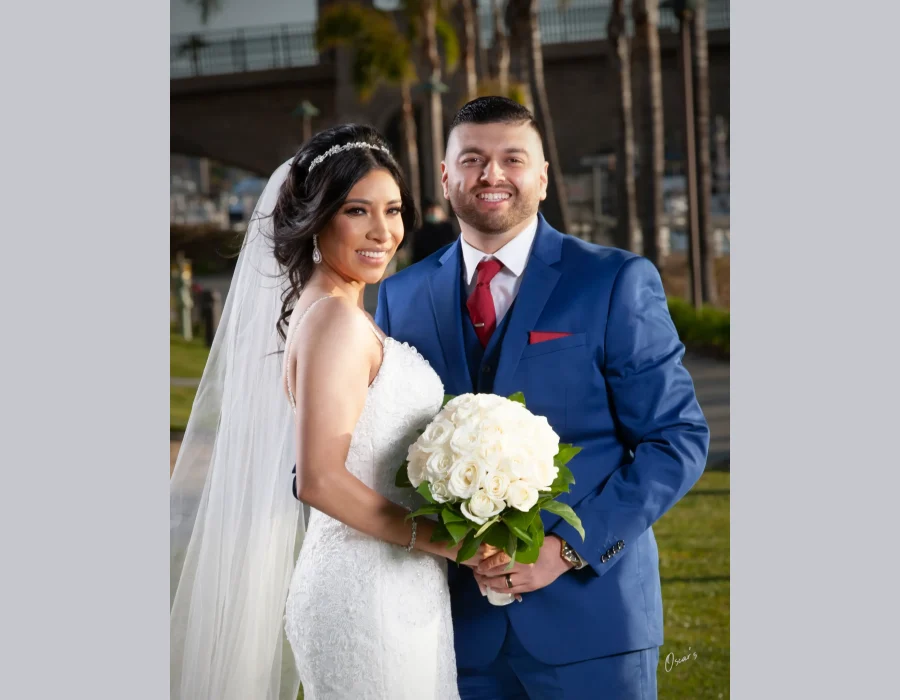 Wedding couple portrait with red tie — bride and groom smiling together outdoors near a marina