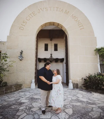 Wedding couple at a historic stone archway — bride and groom holding hands and smiling under an engraved stone archway