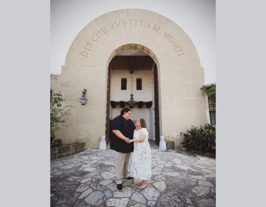Wedding couple at a historic stone archway — bride and groom holding hands and smiling under an engraved stone archway