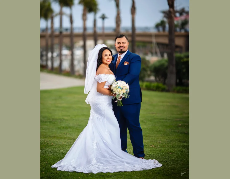 Wedding portrait at church altar — bride and groom smiling together, holding a pink and white bouquet, in front of a gold altar