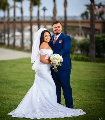 Wedding portrait at church altar — bride and groom smiling together, holding a pink and white bouquet, in front of a gold altar