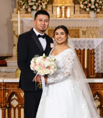 Wedding couple portrait on reception lounge sofa — bride and groom seated together in front of a "Welcome to the Wedding of" sign