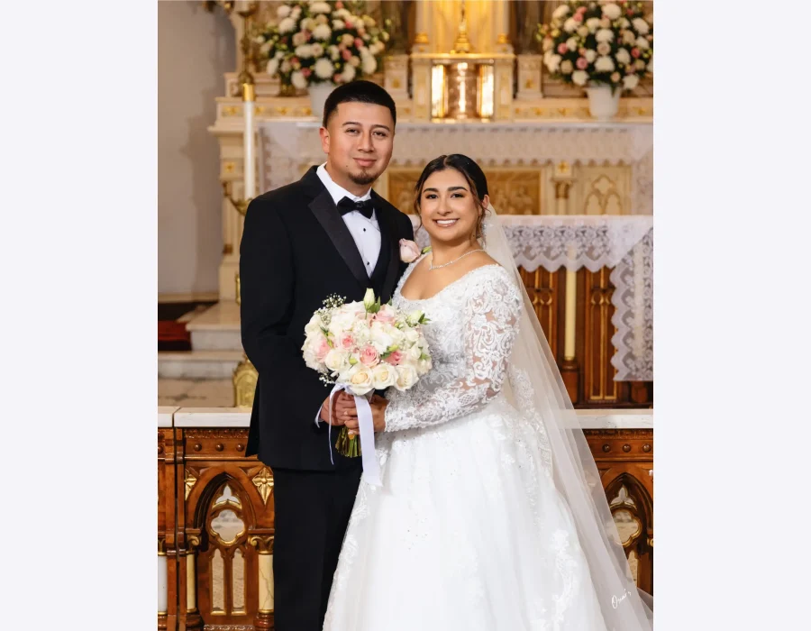 Wedding couple portrait on reception lounge sofa — bride and groom seated together in front of a "Welcome to the Wedding of" sign