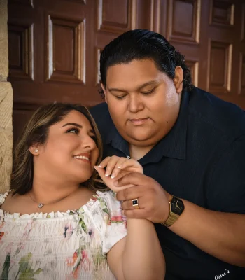 Wedding couple portrait with hands clasped — groom holding bride's hand to his face, wood-paneled background
