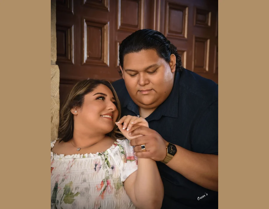 Wedding couple portrait with hands clasped — groom holding bride's hand to his face, wood-paneled background
