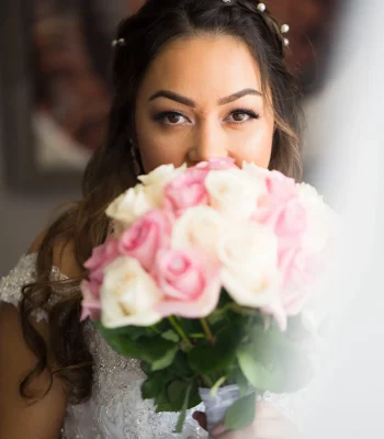 Bride holding bridal bouquet close-up — bride peeking over a bouquet of pink and white roses