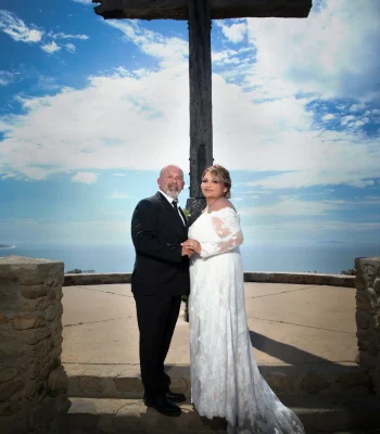 Wedding couple at scenic overlook with cross — couple standing in front of a large wooden cross with ocean view