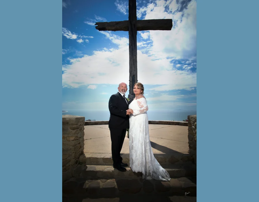 Wedding couple at scenic overlook with cross — couple standing in front of a large wooden cross with ocean view