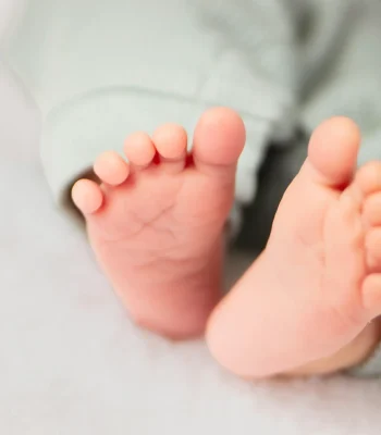 A macro studio photo focusing on the tiny bare feet and wrinkled toes of a newborn baby wearing green pants.