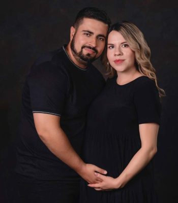 pregnant mother and husband in matching black outfits against a dark studio background