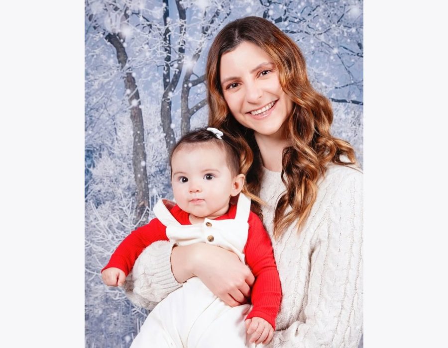 mother holding baby daughter, both dressed in red and white, against a snowy winter backdrop