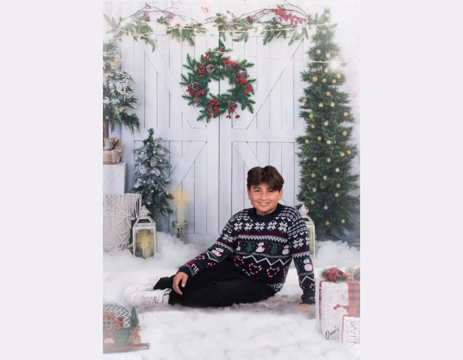 A boy sitting on the floor in a festive holiday sweater next to wrapped gifts and lanterns.