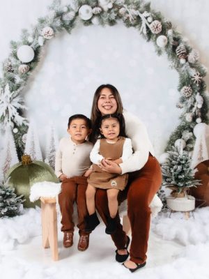 A woman and two children posing together on a snowy bench in front of a large frosted pine wreath arch.