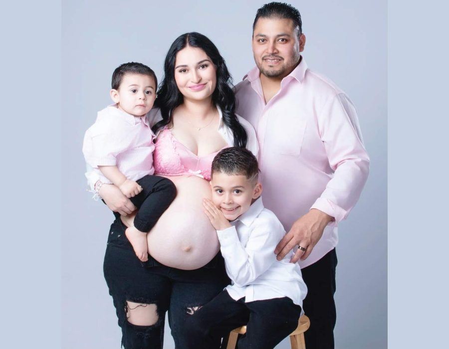 pregnant mother in white lace top, husband, and young son sitting together against a white studio backdrop